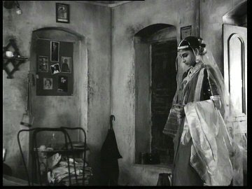 Al día siguiente, y aún vestida de gala, Aparna entra en la destartalada habitación de su ya esposo Apu.
